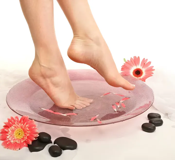 Feet resting over a pedicure bowl with flower petals